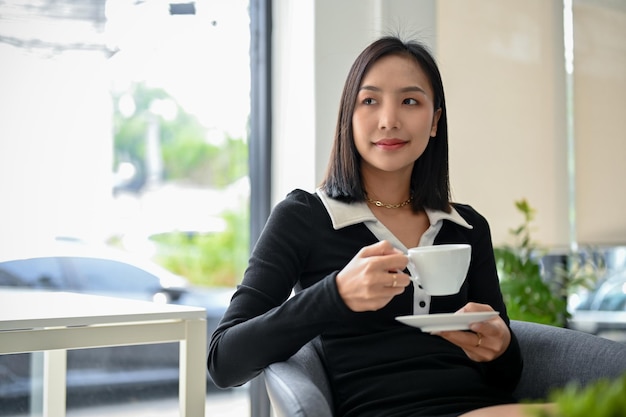 Encantadora mujer de negocios asiática o jefa tomando un café por la tarde en su oficina