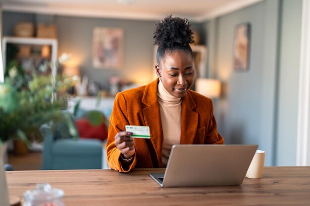 Encantadora mujer de negocios haciendo compras en línea a través de una computadora portátil con tarjeta de crédito en el escritorio de su oficina en casa