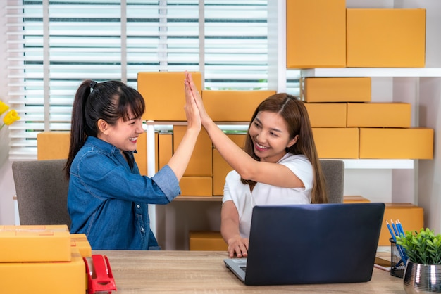 Encantadora mujer de negocios propietaria de dos adolescentes asiáticos trabaja en casa para hacer compras en línea, mirando y emocionada en orden en la computadora portátil y con equipos de oficina, concepto de estilo de vida emprendedor