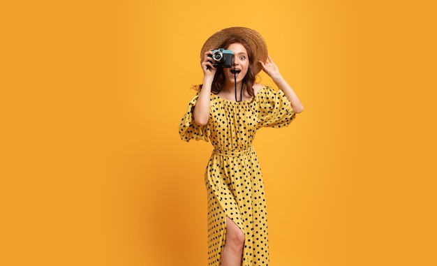 Encantadora mujer pelirroja con sombrero de paja y elegante vestido de verano posando en amarillo
