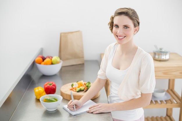 Encantadora mujer de pie en su cocina escribiendo una lista de compras