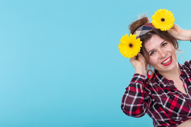 Encantadora mujer positiva joven sonriente en una camisa a cuadros sosteniendo flores de color amarillo brillante en sus manos posando sobre una superficie azul