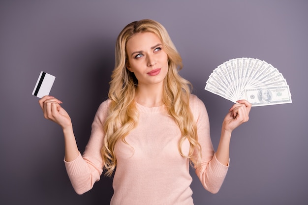 Encantadora mujer rubia en suéter rosa posando con dinero contra la pared púrpura