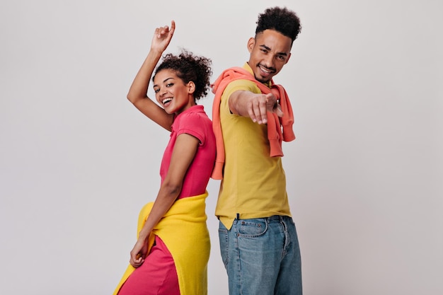 Encantadora mujer y su novio sonriendo y alcanzando la cámara Morena chica de piel oscura y hombre feliz en camiseta amarilla riendo y bailando en aislados