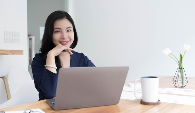 Encantadora mulher asiática trabalhando no escritório usando um laptop olhando para a câmera