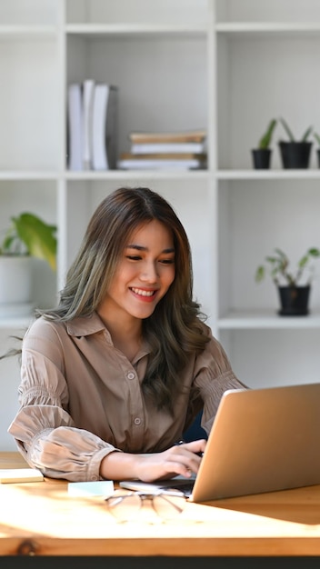 Encantadora mulher criativa trabalhando com computador portátil em seu local de trabalho