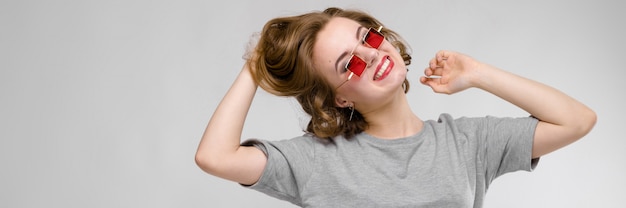 Encantadora mulher jovem em uma camiseta cinza. mulher de óculos vermelhos de olhos quadrados.