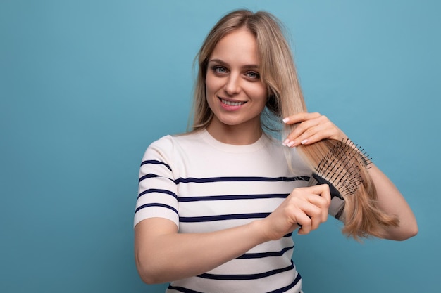 Encantadora mulher loira europeia penteando o cabelo em um fundo azul isolado