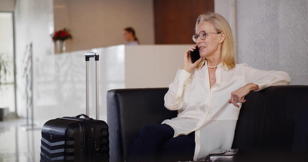 Encantadora mulher sênior falando no celular na sala de espera do hotel