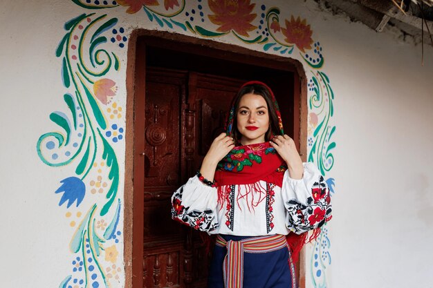 Encantadora mulher sorridente no tradicional colar de lenço ucraniano e vestido bordado em pé no fundo da cabana decorada estilo ucraniano cultura étnica folclórica