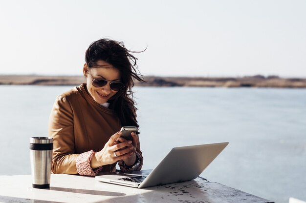 Encantadora mulher trabalhando fora, digitando uma mensagem no celular