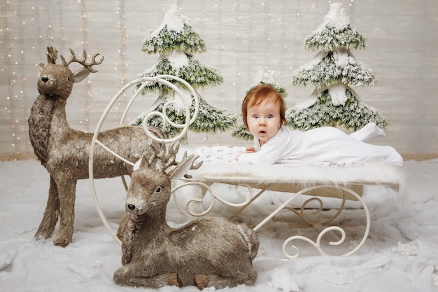 Encantadora niña acostada en trineo de nieve de Navidad alrededor de los ciervos, Foto de estudio.