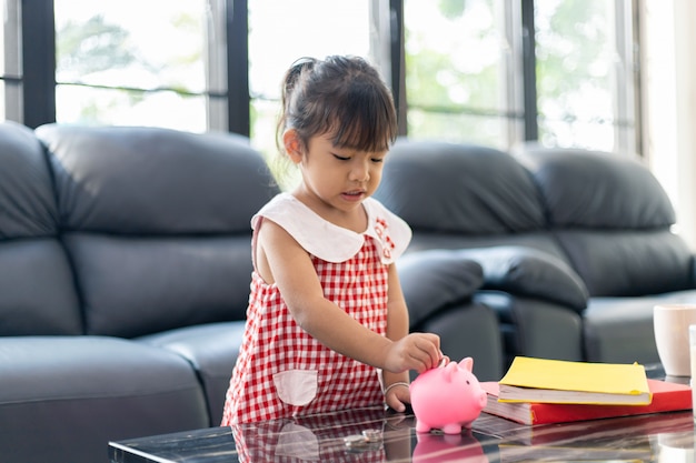 Foto encantadora niña asiática poniendo dinero en la hucha para ahorrar