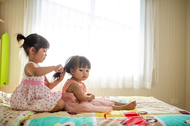 Encantadora niña cepillando el cabello de su hermana mientras está sentada en la cama