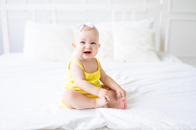 Encantadora niña en un dormitorio blanco y soleado Un bebé recién nacido descansa en la cama Textiles y ropa de cama para niños Mañana familiar en casa Un bebé recién nacido está sentado en la cama después de dormir