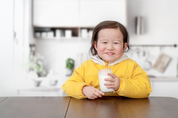 encantadora niña está desayunando y bebiendo yogur con una cuchara