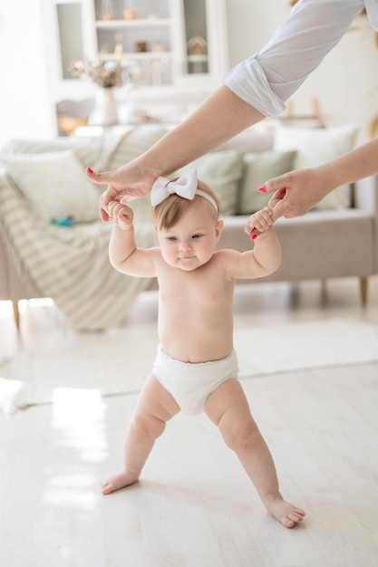 Una encantadora niña en pañales da sus primeros pasos en casa de la mano de su madre un niño aprende a caminar en casa en una luminosa sala de estar un niño sano en casa