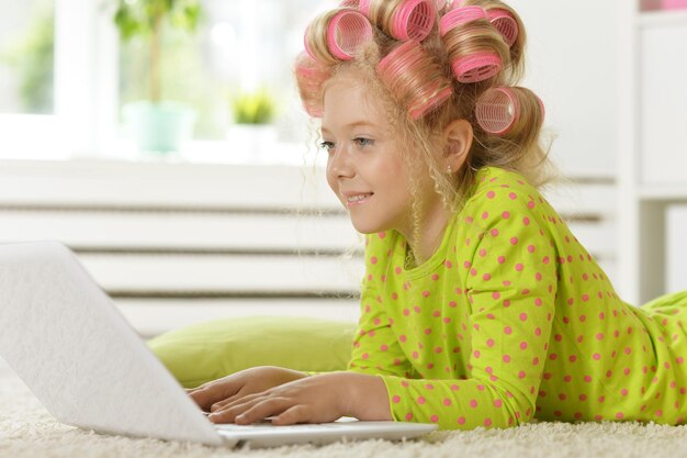 Encantadora niña con rulos rosas usando laptop