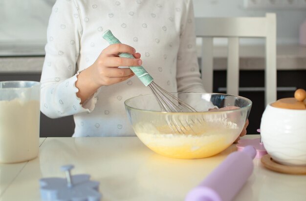 Foto una encantadora niña de siete años está aprendiendo a cocinar en una cocina blanca. un niño feliz cocina, hace masa, hornea galletas. un pequeño ayudante ayuda en la cocina.