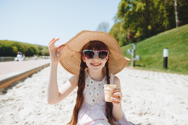 Encantadora niña con sombrero come helado en la playa de la playa Concepto de vacaciones de verano