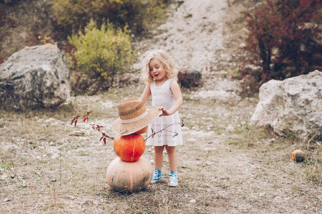 encantadora niña en un sombrero de paja, silla de mimbre, calabazas, otoño