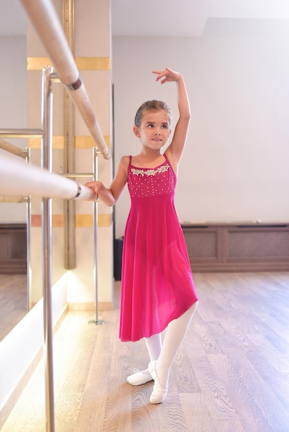 Encantadora niña sueña con convertirse en bailarina La niña del vestido rosa está bailando agarrándose a la barraLa niña está estudiando ballet