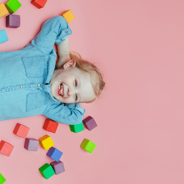 Una encantadora niña vestida de mezclilla con cubos de colores de madera y riendo.