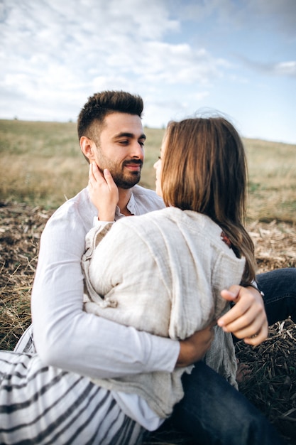 Encantadora pareja abrazándose, besándose y sonriendo contra el cielo sentado en el césped