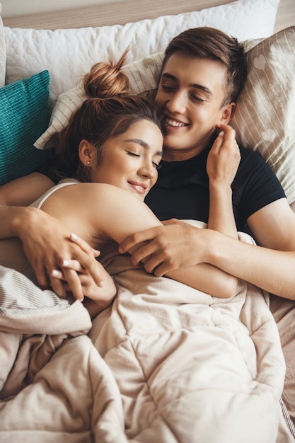 Encantadora pareja acostada en la cama y abrazar en la mañana sonriendo con los ojos cerrados