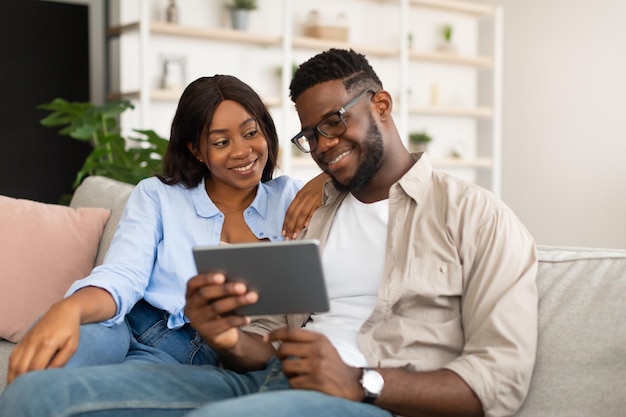 Encantadora pareja afroamericana sentada en un sofá usando una tableta
