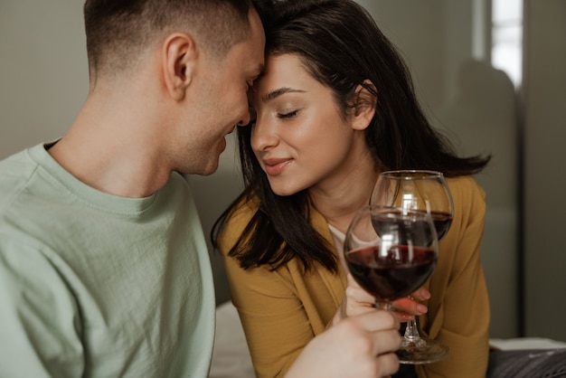 Encantadora pareja con copas de vino tiene una cena romántica en casa. Familia joven feliz se mudó a un nuevo apartamento.