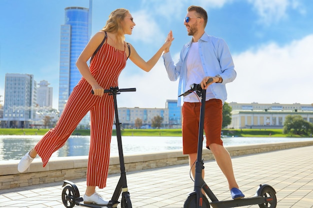 Encantadora pareja divirtiéndose conduciendo scooter eléctrico a lo largo del paseo marítimo de la ciudad