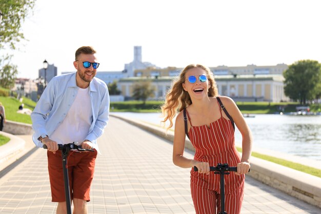 Encantadora pareja divirtiéndose conduciendo scooter eléctrico por el paseo de la ciudad.