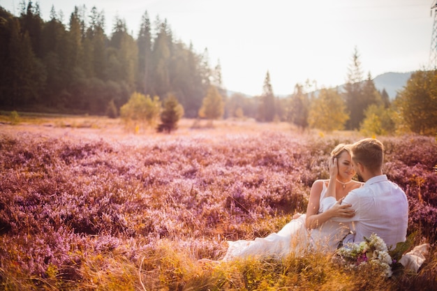 La encantadora pareja de enamorados abrazándose y sentándose en la hierba