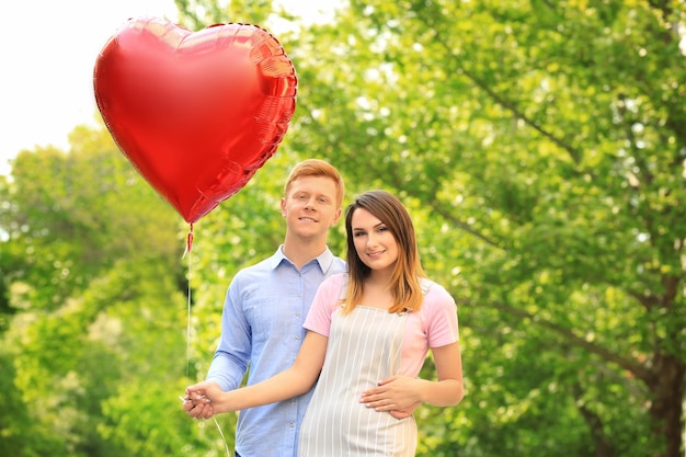 Encantadora pareja con globo en forma de corazón en el parque en un día soleado