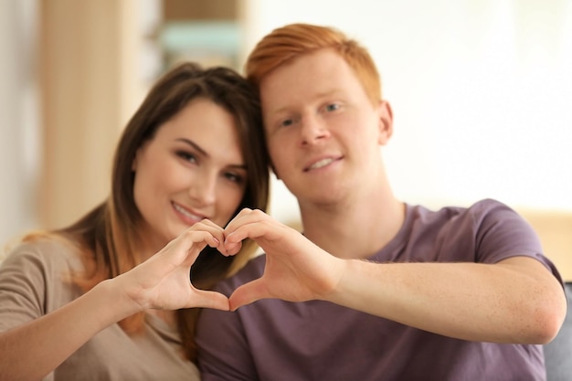 Encantadora pareja haciendo corazón con las manos en casa