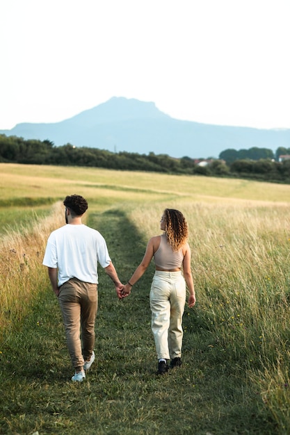 Encantadora pareja heterosexual en un campo de hierba caminando y besándose