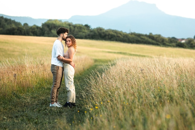 Encantadora pareja heterosexual en un campo de hierba caminando y besándose