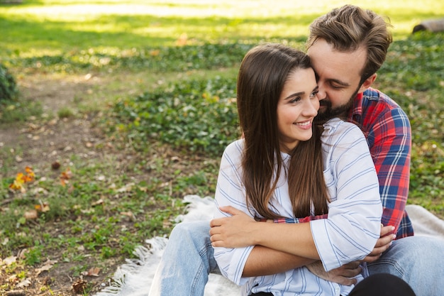 Encantadora pareja hombre y mujer vestidos con ropa casual abrazando mientras descansa en el parque verde