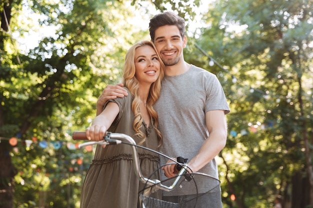 Encantadora pareja joven complacida posando junto con bicicleta