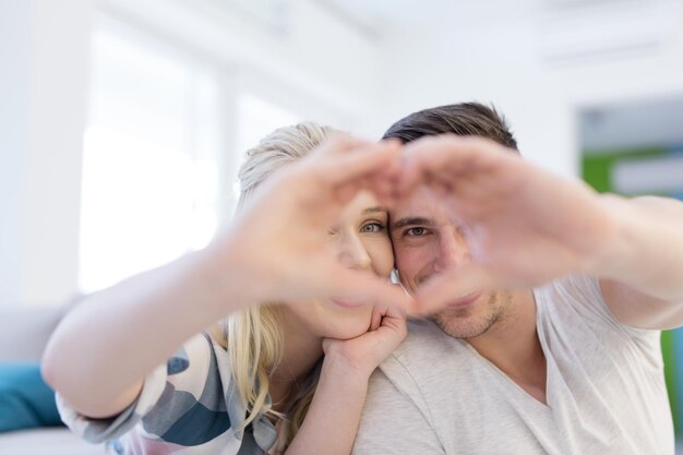 Encantadora pareja joven haciendo corazón con las manos en casa