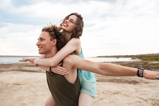 Encantadora pareja joven pasar tiempo divertido en la playa, paseo en caballito