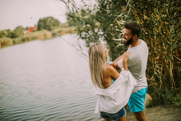 Encantadora pareja joven pescando junto a un lago