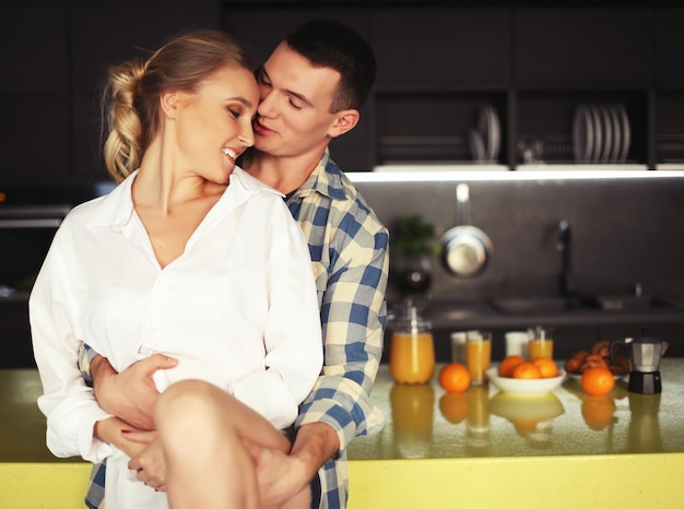 Encantadora pareja joven de pie y abrazándose en una cocina en casa