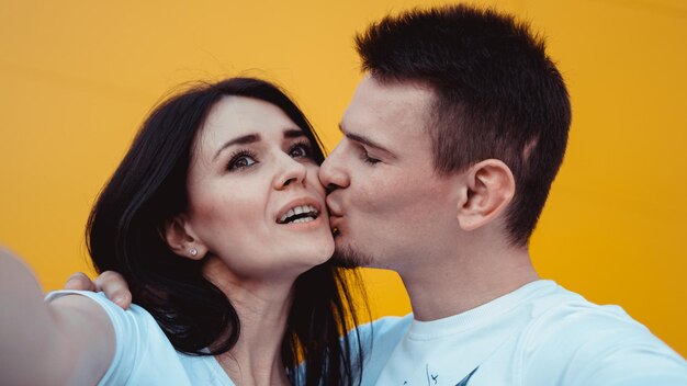 Encantadora pareja joven posando juntos mientras hace selfie en smartphone sobre fondo amarillo