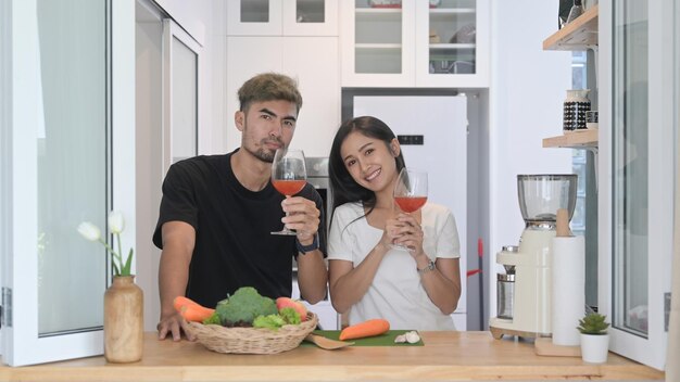 Encantadora pareja joven preparando comida saludable y bebiendo vino en la cocina de casa