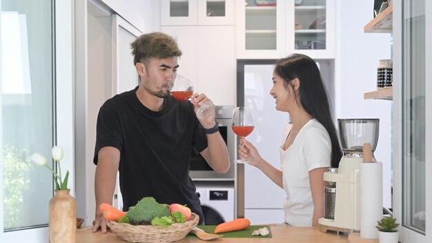 Encantadora pareja joven preparando comida saludable y bebiendo vino en la cocina casera moderna