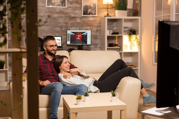 Foto encantadora pareja joven relajándose en el sofá y viendo una película en la televisión por la noche