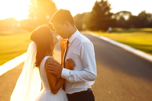 Foto encantadora pareja de novios al atardecer novia novio en traje de novia con ramo de flores romántico