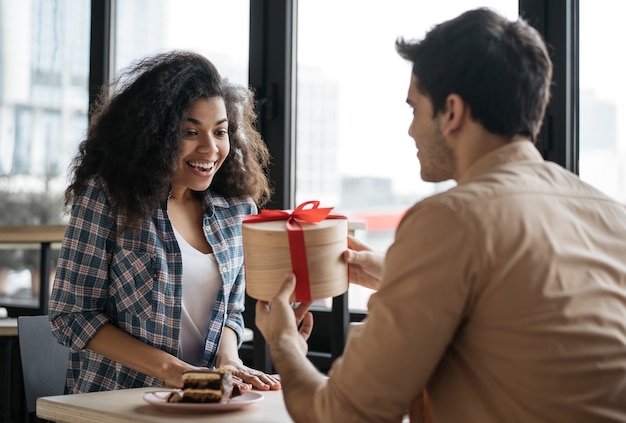 Encantadora pareja sentada en el café hombre dando regalo de cumpleaños